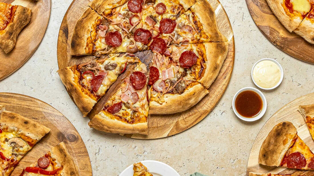 Overhead view of assorted pizzas on wooden boards with dipping sauces on a stone table at an nsw event.
